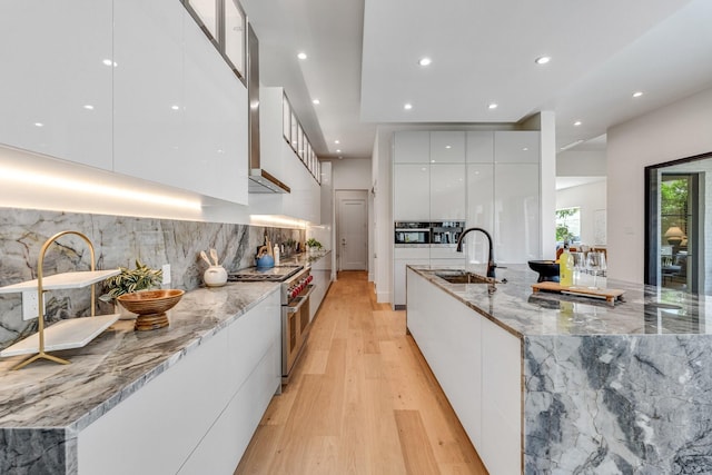 kitchen with modern cabinets, a sink, double oven range, white cabinetry, and light wood-style floors