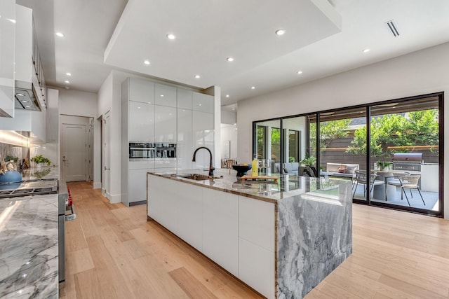 kitchen featuring modern cabinets, a sink, gas range, white cabinetry, and light wood-style flooring