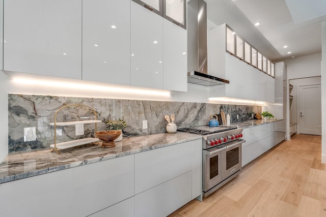 kitchen with modern cabinets, range with two ovens, wall chimney exhaust hood, white cabinets, and recessed lighting