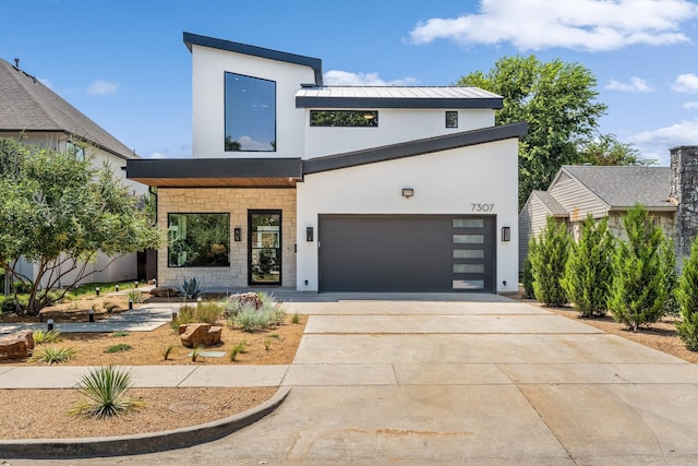 contemporary home with a garage, driveway, a standing seam roof, stucco siding, and metal roof