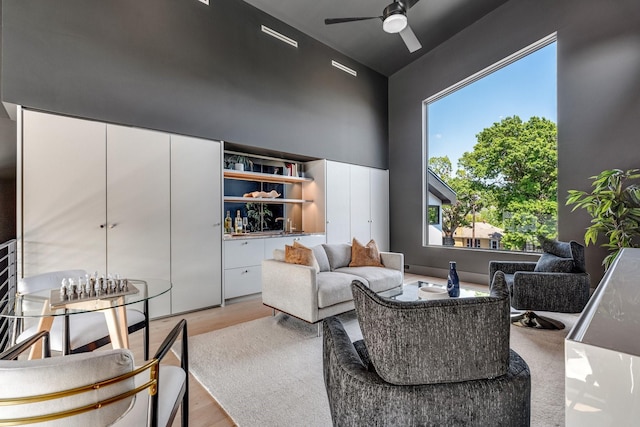 living area featuring a ceiling fan, light wood finished floors, and a towering ceiling