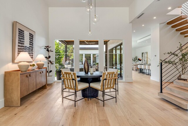 dining space featuring stairs, light wood-style floors, plenty of natural light, a towering ceiling, and baseboards