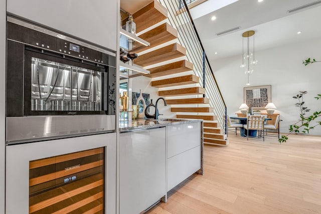 bar area featuring wine cooler, stairway, light wood-type flooring, a towering ceiling, and wall oven