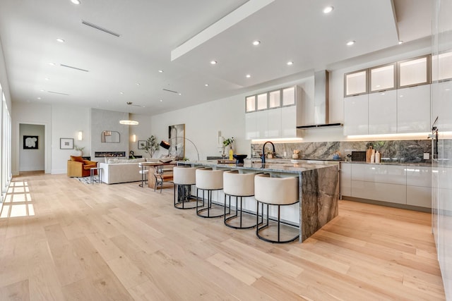 kitchen with wall chimney exhaust hood, modern cabinets, white cabinetry, a breakfast bar, and recessed lighting