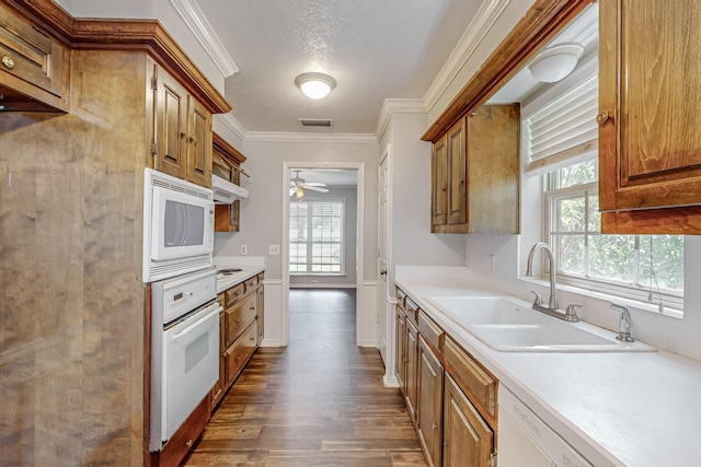 kitchen featuring white appliances, a sink, brown cabinetry, dark wood-style flooring, and crown molding