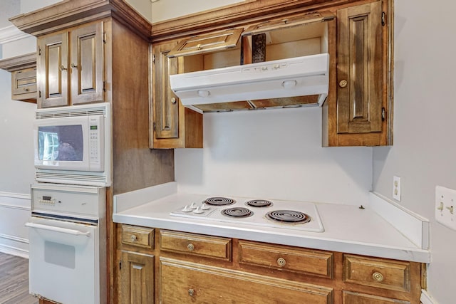 kitchen featuring white appliances, under cabinet range hood, brown cabinets, and light countertops