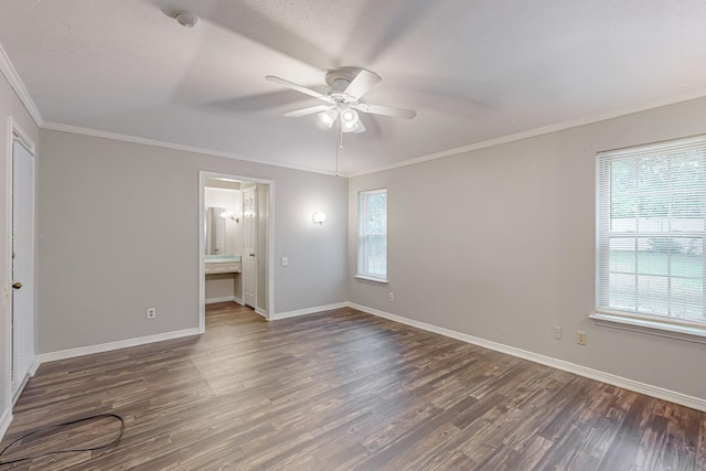 unfurnished bedroom featuring wood finished floors, crown molding, baseboards, ensuite bathroom, and a ceiling fan