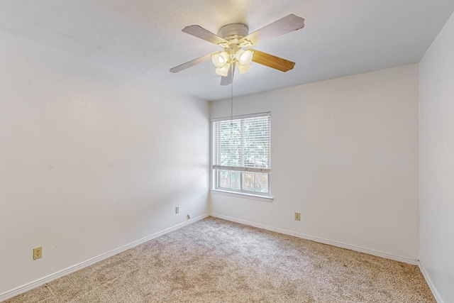carpeted spare room featuring baseboards and a ceiling fan
