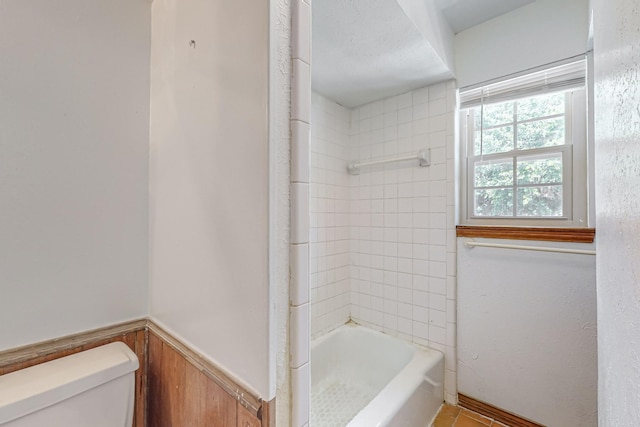 bathroom with toilet, wainscoting, and tub / shower combination