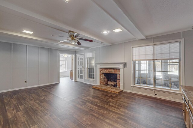 unfurnished living room featuring a fireplace, beamed ceiling, ceiling fan, dark wood-style flooring, and a decorative wall