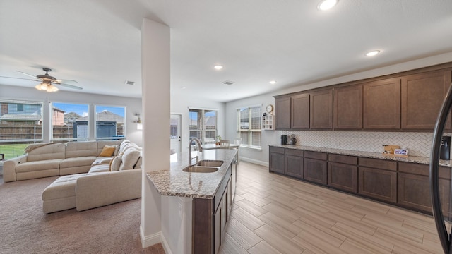 kitchen featuring a sink, baseboards, decorative backsplash, light stone counters, and ceiling fan