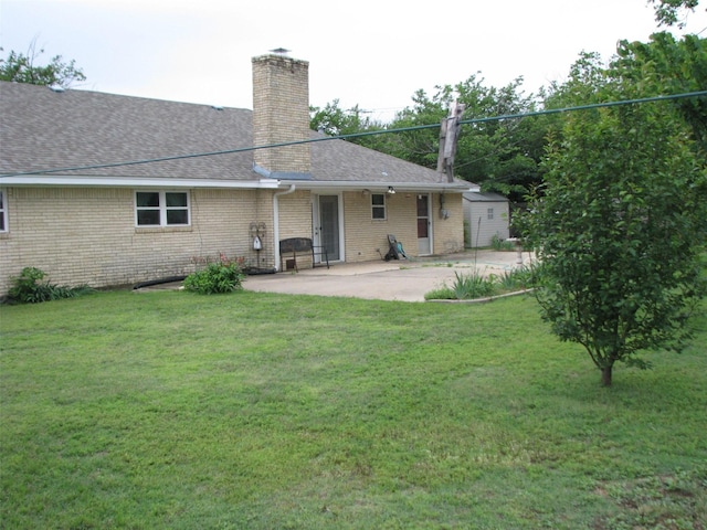 rear view of property with a patio area, a chimney, roof with shingles, brick siding, and a lawn