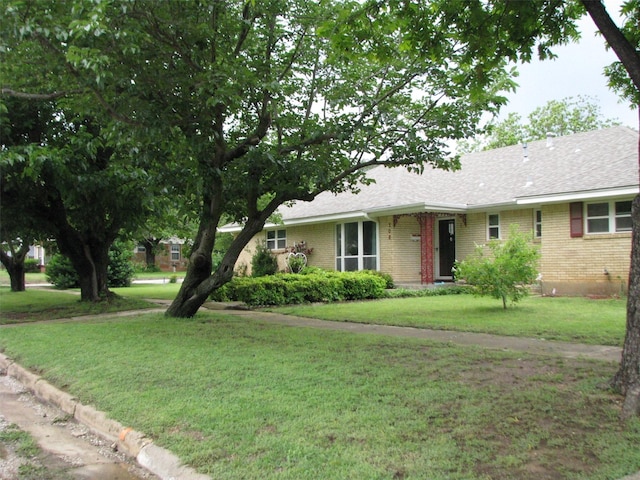 ranch-style home featuring brick siding, a front yard, and roof with shingles