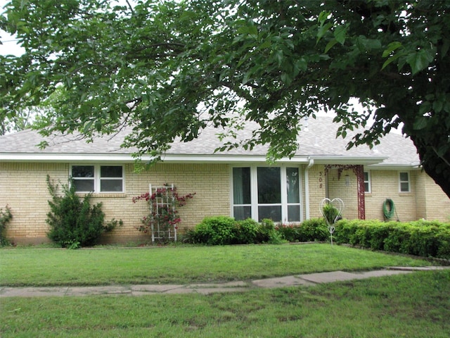 ranch-style home with brick siding, a front lawn, and roof with shingles