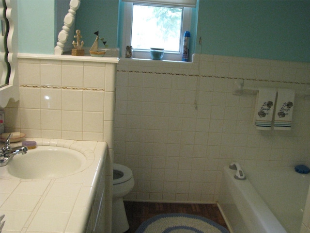 full bathroom with tile walls, a sink, toilet, a tub to relax in, and a wainscoted wall