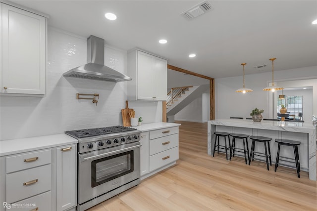 4131 Waller Dr, Shreveport, LA 71119 - kitchen with high end range, wall chimney exhaust hood, a breakfast bar area, light wood finished floors, and white cabinetry