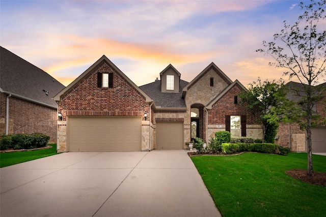 french provincial home with brick siding, driveway, stone siding, a lawn, and a garage