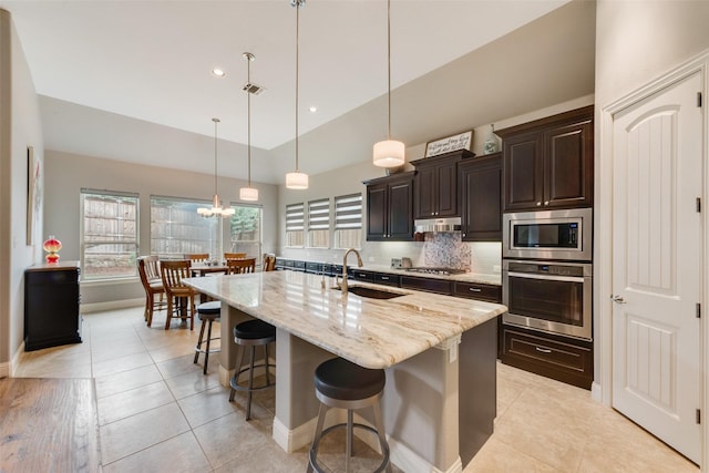 kitchen with appliances with stainless steel finishes, a sink, a breakfast bar area, light tile patterned floors, and high vaulted ceiling