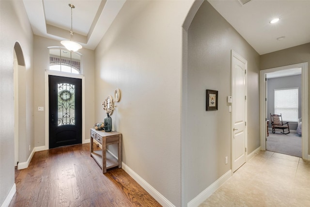 entrance foyer with arched walkways, baseboards, a raised ceiling, and light wood-style flooring
