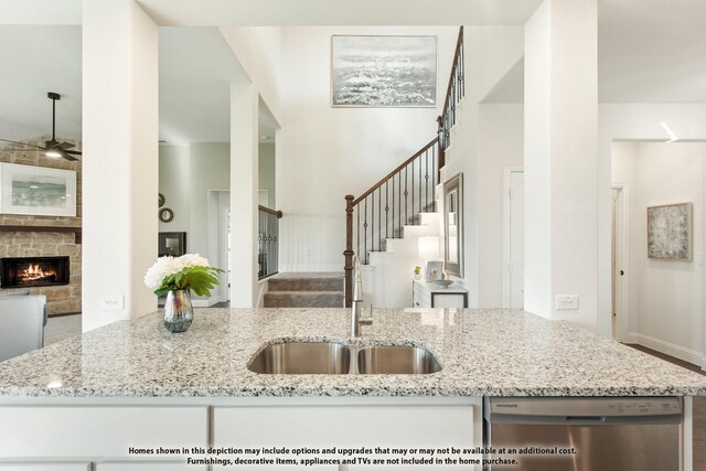 kitchen featuring stainless steel dishwasher, open floor plan, a ceiling fan, light stone counters, and a stone fireplace