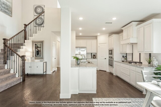 kitchen featuring stainless steel appliances, dark wood-type flooring, a sink, light stone counters, and white cabinetry