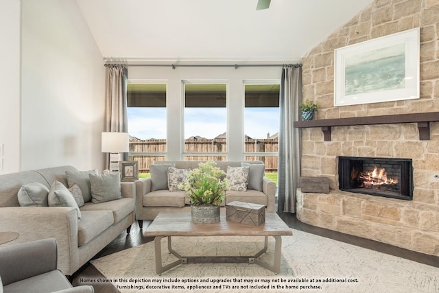 living room with lofted ceiling, a stone fireplace, wood finished floors, and healthy amount of natural light