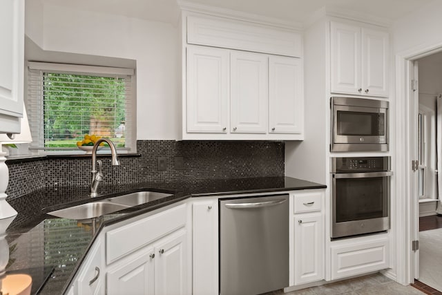 kitchen featuring appliances with stainless steel finishes, a sink, white cabinetry, backsplash, and dark stone counters