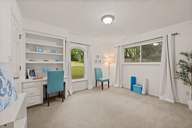 office area featuring light carpet, a textured ceiling, baseboards, and built in desk