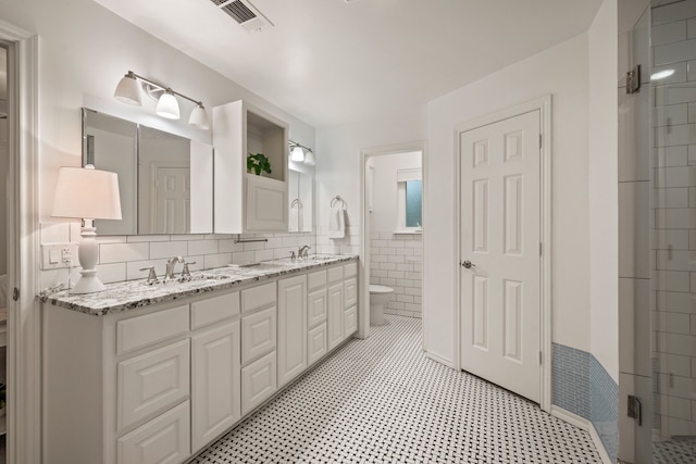 bathroom featuring toilet, tile walls, double vanity, and a stall shower