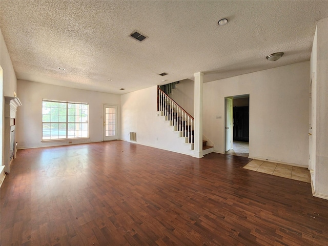 unfurnished living room with a textured ceiling, dark wood-style flooring, healthy amount of natural light, a tile fireplace, and baseboards