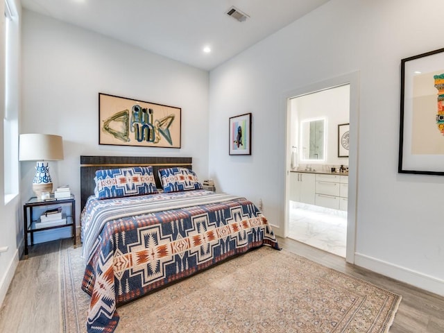 bedroom featuring wood finished floors, baseboards, ensuite bath, and recessed lighting
