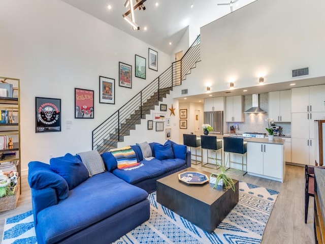 living room with stairway, a towering ceiling, light wood-style floors, and recessed lighting