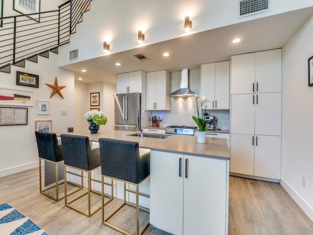 kitchen with freestanding refrigerator, wall chimney exhaust hood, a sink, light wood finished floors, and baseboards