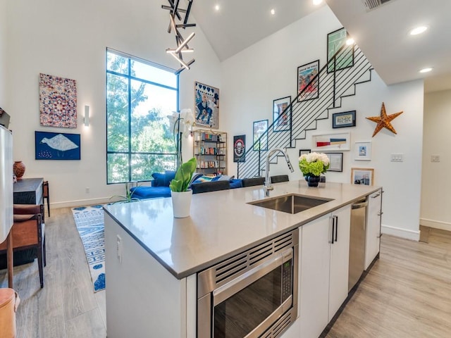 kitchen with a sink, appliances with stainless steel finishes, an island with sink, open floor plan, and high vaulted ceiling