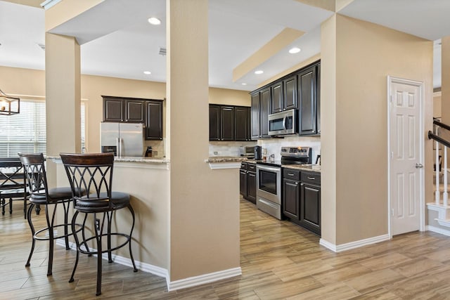2499 Streamside Ct, Frisco, TX 75036 - kitchen featuring stainless steel appliances, decorative backsplash, a kitchen bar, light wood-type flooring, and recessed lighting