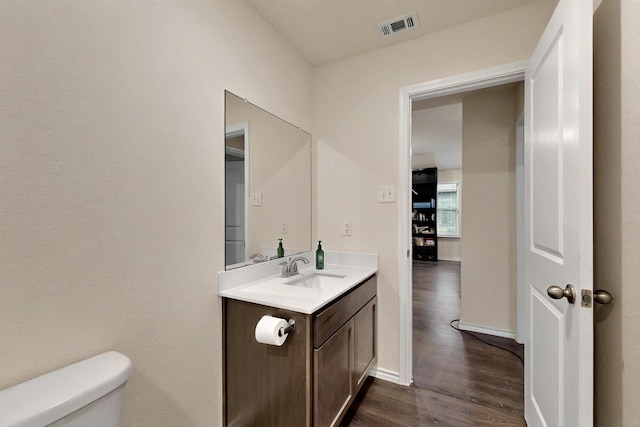 half bath featuring wood finished floors, vanity, toilet, and baseboards