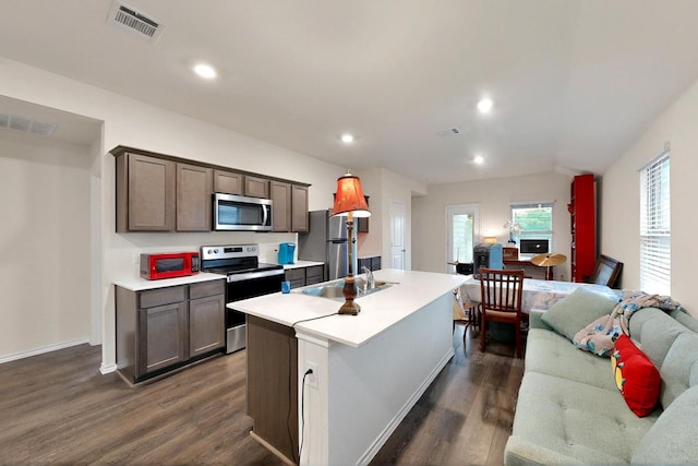 kitchen with appliances with stainless steel finishes, a sink, dark wood-style floors, a kitchen island with sink, and light countertops