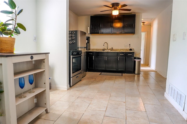 kitchen featuring a sink, a ceiling fan, light stone countertops, stainless steel range with gas cooktop, and dark cabinets