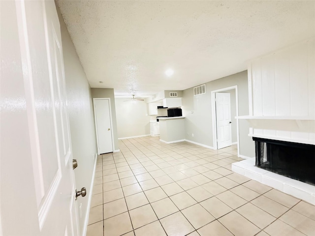 unfurnished living room featuring a multi sided fireplace, light tile patterned floors, a textured ceiling, ceiling fan, and baseboards