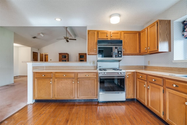 kitchen with gas range, light countertops, ceiling fan, vaulted ceiling, and a peninsula