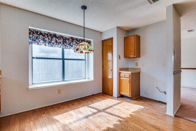 unfurnished dining area featuring light wood-type flooring, a textured ceiling, and wallpapered walls