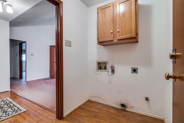 laundry area featuring electric dryer hookup, cabinet space, hookup for a washing machine, light wood finished floors, and a textured ceiling