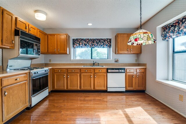 kitchen featuring white appliances, wallpapered walls, a sink, light countertops, and light wood-style flooring