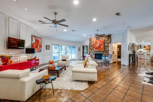 living room featuring ceiling fan, a decorative wall, a stone fireplace, lofted ceiling, and recessed lighting
