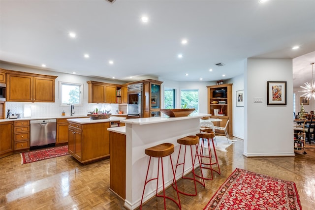 kitchen featuring appliances with stainless steel finishes, a center island, brown cabinets, light countertops, and baseboards
