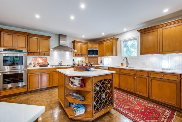 kitchen featuring wall chimney range hood, stainless steel appliances, a sink, light countertops, and brown cabinetry
