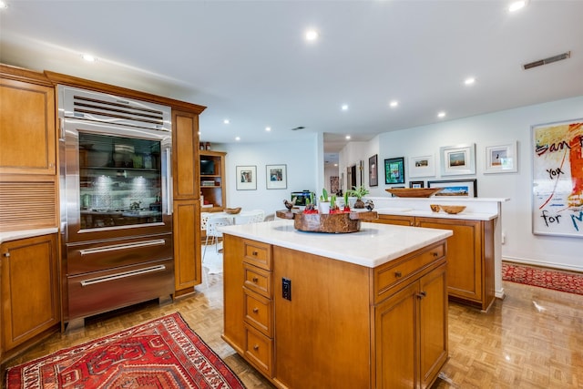 kitchen featuring a kitchen island, built in refrigerator, brown cabinets, light countertops, and recessed lighting