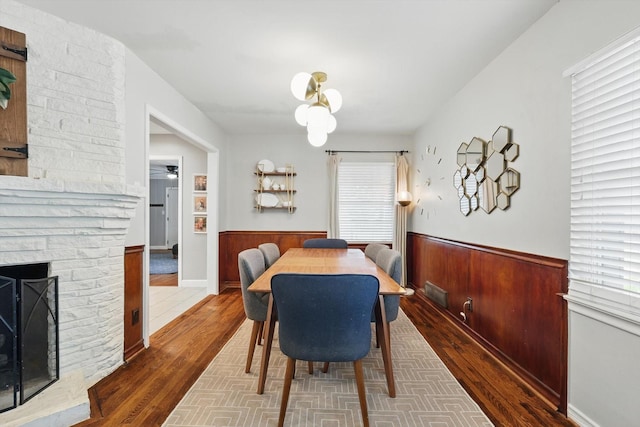 dining room with wainscoting, wood finished floors, ceiling fan, and a fireplace