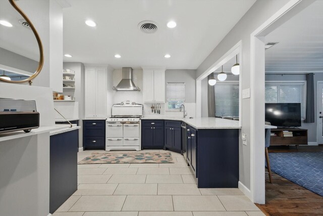 kitchen with range with two ovens, wall chimney range hood, blue cabinets, light countertops, and a sink