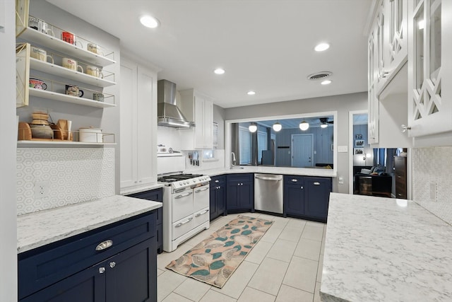 kitchen featuring dishwasher, wall chimney range hood, range with two ovens, blue cabinetry, and a sink